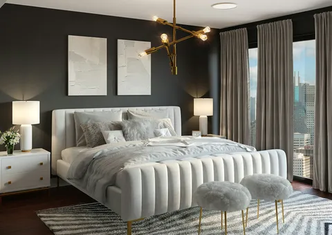 A modern bedroom with a white upholstered bed, gold chandelier, and city view